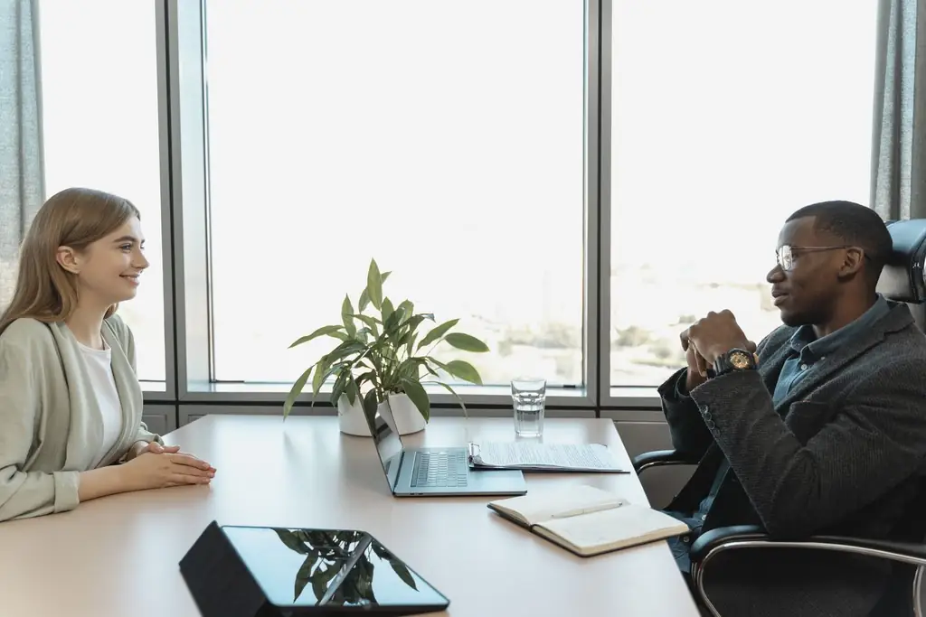 A hiring manager and a candidate talking across a desk in a bright office