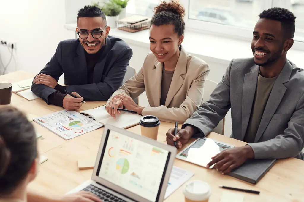 A team of colleagues smiling around a meeting table with printed reports and a laptop